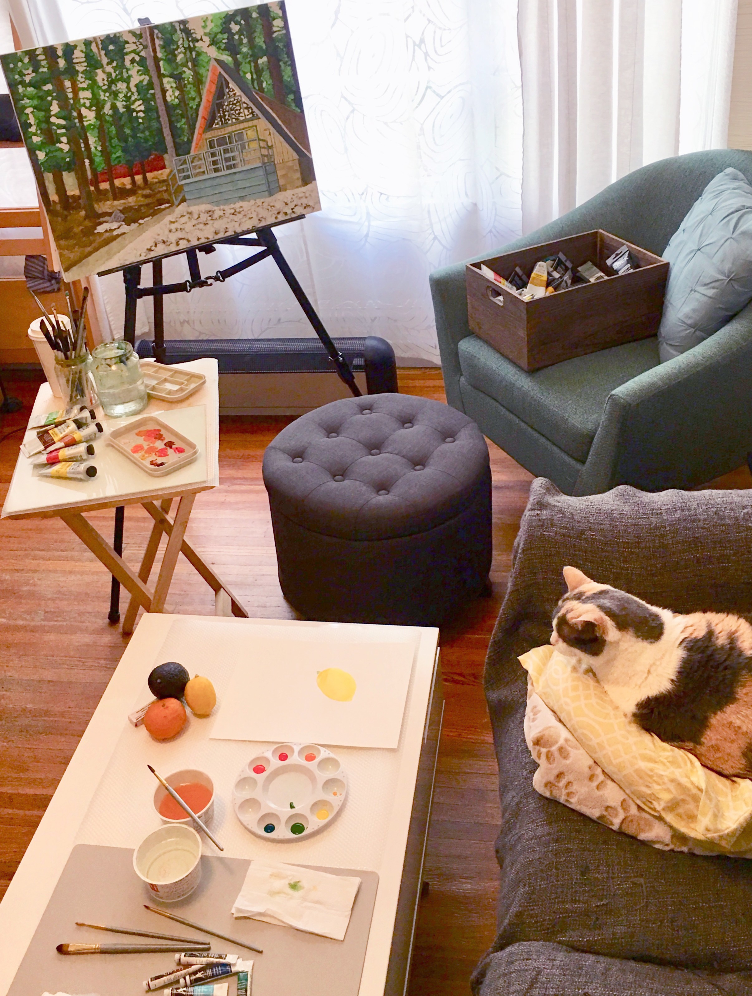 Living room with a painting on an easel, paints, palettes and brushes with a cat